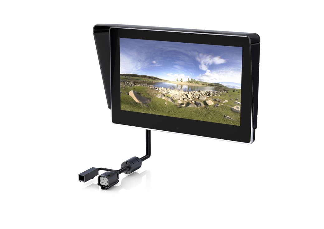 A black monitor with a sunshade displays an outdoor scene featuring green fields, a rocky area, and a blue sky with white clouds. Attached to the monitor is a cable with connectors. The setup is isolated on a white background.