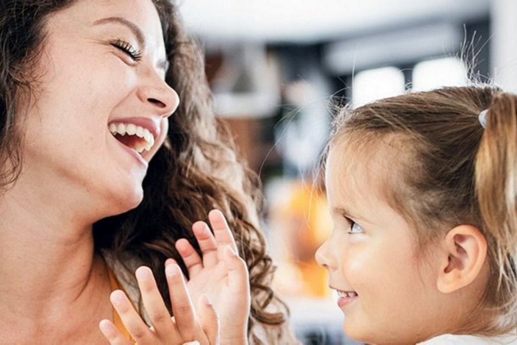 A young mother holds her daughter in her arms and they both smile.