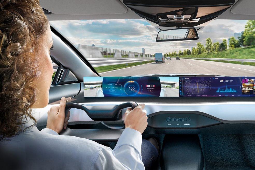 A woman sits at the wheel of a futuristic concept car and drives along a highway