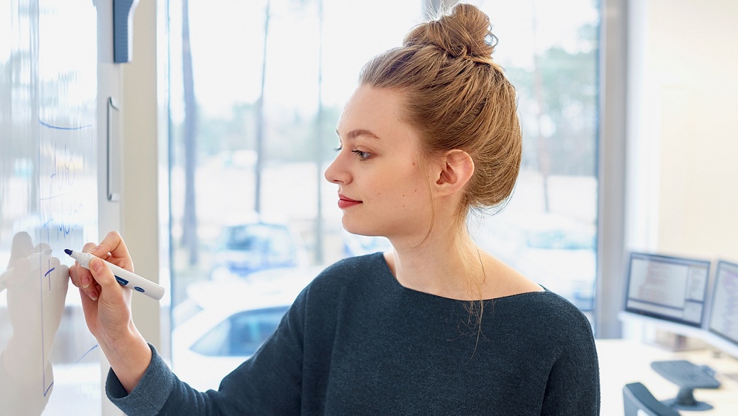a young woman with red hair and red lipstick stands in front of a white board and writes something on it